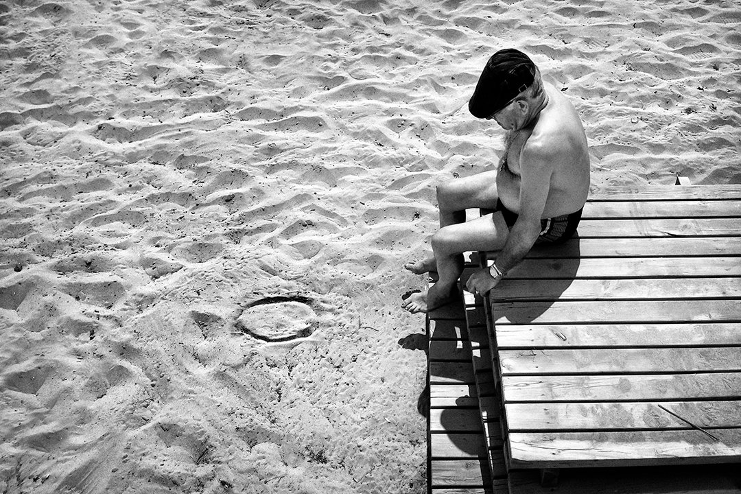 A man sitting on the edge of a wooden walkway over the sand.